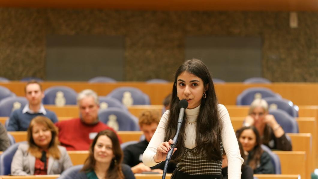 Een jonge bezoeker spreekt andere bezoekers toe achter de interruptiemicrofoon tijdens de actieve ledendag in de Tweede Kamer